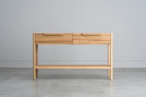 Dieser Beistelltisch aus massiver Eiche verbindet Funktionalität mit elegantem Design. Es hat zwei praktische Schubladen mit charakteristischen gerillten Fronten und minimalistischen Griffen, die ihm einen modernen Look verleihen.