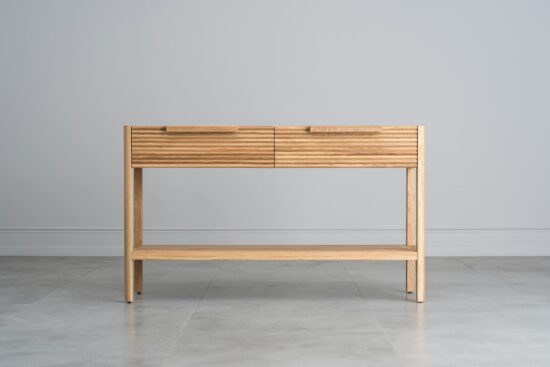 Dieser Beistelltisch aus massiver Eiche verbindet Funktionalität mit elegantem Design. Es hat zwei praktische Schubladen mit charakteristischen gerillten Fronten und minimalistischen Griffen, die ihm einen modernen Look verleihen.