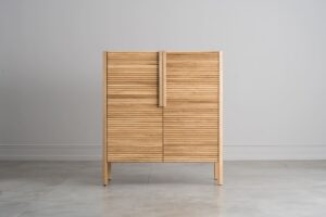 Dieser Schrank besticht durch seine einzigartige, gewellte Türfront, abgerundete Kanten, leichte, minimalistische Beine und elegante Holzgriffe, die zusammen ein harmonisches, modernes und funktionales Design ergeben.