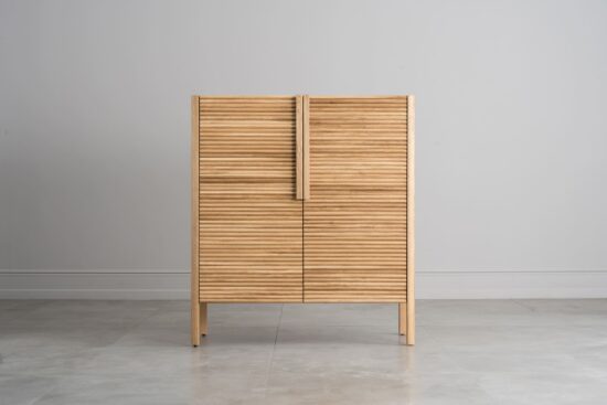 Dieser Schrank besticht durch seine einzigartige, gewellte Türfront, abgerundete Kanten, leichte, minimalistische Beine und elegante Holzgriffe, die zusammen ein harmonisches, modernes und funktionales Design ergeben.