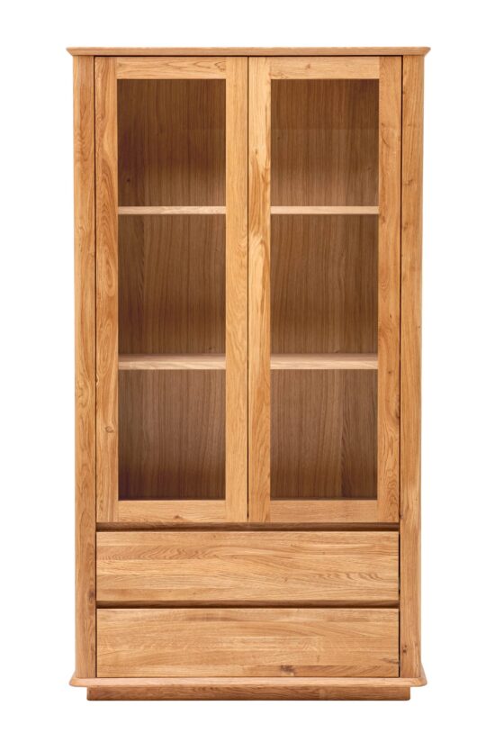 Der Wohnzimmerschrank Celin aus massiver Eiche verbindet die Eleganz einer Vitrine mit der Praktikabilität von Schubladen. Dank seiner klaren Linien, Kurven und der natürlichen Holzmaserung wirkt er zeitlos und macht jede Einrichtung gemütlich.